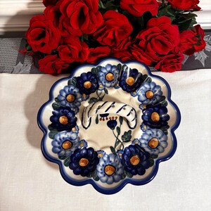May include: A ceramic serving plate with a scalloped edge, decorated with blue floral patterns. The plate has a white base with a blue rim and a handle. The flowers are in shades of blue and have yellow centers. The plate is approximately 10 inches in diameter.
