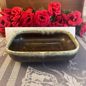 May include: A dark green glazed ceramic dish with a light green rim. The dish is rectangular and has a slightly rounded bottom.