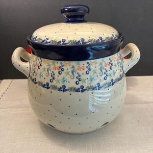 May include: A ceramic garlic keeper with a lid, featuring a cream-colored base with blue polka dots and a band of colorful sea life patterns including seahorses, starfish, and fish. It has two side handles and ventilation holes at the base.