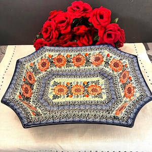 May include: A rectangular ceramic serving bowl with scalloped edges, featuring a cream-colored base decorated with vibrant orange floral patterns, green leaves, and intricate dark blue and black speckled borders throughout the interior surface.