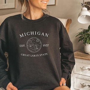 May include: Black sweatshirt with a white graphic design that says "MICHIGAN EST. 1837 GREAT LAKES STATE" with a stylized image of a lake and sailboats.