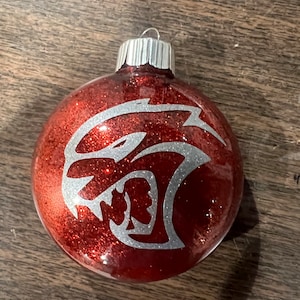 May include: Red Christmas ornament with a silver glitter finish and a silver silhouette of a snarling animal head.