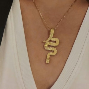 Peut inclure: Un collier en chaîne dorée avec un pendentif en forme de serpent. Le serpent est enroulé et a une surface texturée.