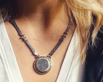 Pode incluir: Um colar de corrente de prata com um pingente redondo que apresenta um design detalhado em preto e dourado.