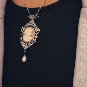 May include: A silver cameo necklace with a pearl pendant. The cameo features a detailed profile of a woman in a delicate frame.