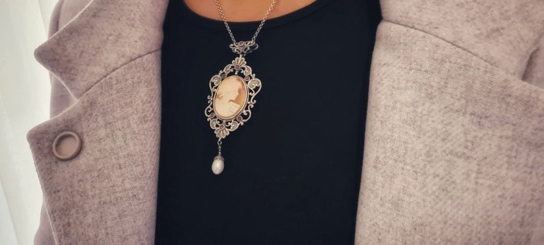 May include: A silver cameo necklace with a pearl pendant. The cameo features a detailed profile of a woman in a delicate frame.