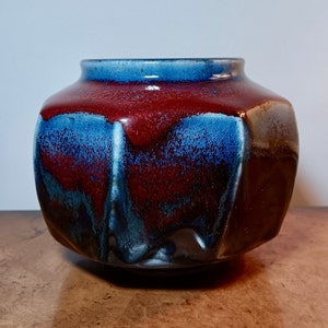 May include: A dark red and blue ceramic vase with a textured glaze. The vase has a rounded body and a wide opening.