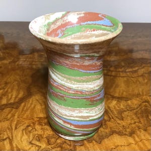 Könnte beinhalten: Eine Keramikvase mit einem Marmormuster in Braun-, Grün-, Weiß- und Blautönen. Die Vase hat eine breite Öffnung und einen schmalen Boden.