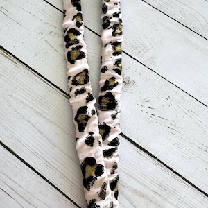 May include: A pink and white lanyard with a leopard print design. The lanyard has black and gold spots and a metal clasp with a key ring.