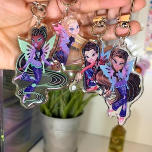 May include: Four clear acrylic keychains featuring stylised cartoon characters with fairy wings, dark hair, and purple outfits. Each keychain has a silver-toned metal lobster clasp attached to the top, showcasing detailed character illustrations.