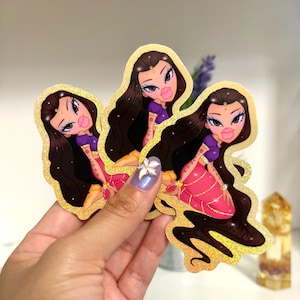 May include: Three stickers featuring a cartoon woman with long dark hair, large lips, and a purple top. The stickers have a gold glitter border and are held in a hand. The woman is wearing a pink and gold outfit.