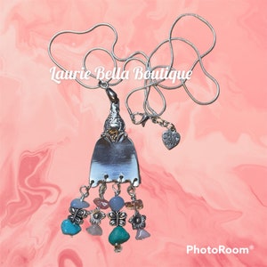 Può includere: Una collana d'argento con un ciondolo a forma di forchetta vintage e un ciondolo che dice "fatto con amore". Il ciondolo è decorato con perline di pietre preziose turchesi, rosa e marroni e ciondoli a forma di farfalla.