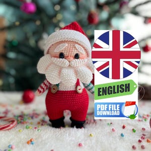 Puede incluir: Una muñeca de Papá Noel de ganchillo con gorro y pantalón rojos, barba y bigote blancos y cara color crema. La muñeca tiene ojos negros y lleva un gorro blanco. La imagen incluye una etiqueta que dice "ENGLISH" y "PDF FILE DOWNLOAD".