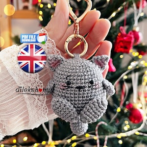 May include: A handmade grey crochet cat keyring with a gold-coloured heart-shaped clasp. The cat has pink accents on its ears and cheeks. A Union Jack button and the text "PDF FILE DOWNLOAD" are also visible.