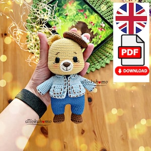 Könnte beinhalten: Ein gehäkeltes Stofftierbär, der eine blaue Jeansjacke und braune Stiefel trägt. Der Bär hat einen braunen Hut mit einer weißen Blume oben drauf. Der Bär hält ein Herz in seinen Pfoten. Der Text "dilekshome" ist im Bild sichtbar.