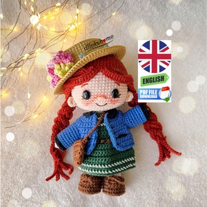 May include: Crochet amigurumi doll with red hair, a blue jacket, a green dress, and a brown hat with flowers. The doll is holding a brown bag. The image includes the text "ENGLISH PDF FILE DOWNLOAD".
