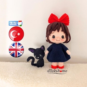 Puede incluir: Muñeca y gato negro de ganchillo. La muñeca tiene cabello castaño, un lazo rojo, un vestido azul marino y zapatos rojos. El gato negro tiene orejas moradas. Incluye el texto "dilekshome".