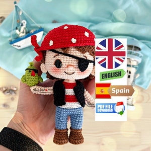 Puede incluir: Muñeca pirata amigurumi de crochet con una camisa a rayas rojas y blancas, pantalones vaqueros azules y un parche en el ojo marrón. La muñeca sostiene un loro verde. La muñeca lleva un sombrero de pirata de crochet rojo y blanco.