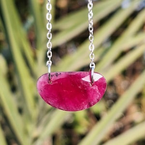 May include: A silver chain necklace with a pink, teardrop-shaped gemstone pendant.