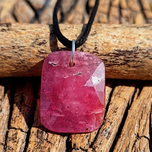 May include: A pink gemstone pendant on a black cord necklace. The gemstone is faceted and has a shiny, polished finish.