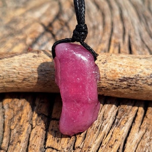 May include: A pink, irregularly shaped stone pendant on a black cord necklace. The pendant is smooth and shiny, and the cord is thin and delicate.