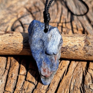 Può includere: Un ciondolo in pietra blu e argento su un cordino nero. La pietra ha una forma irregolare e una texture ruvida e naturale.