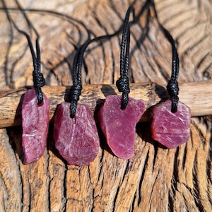 Puede incluir: Cuatro colgantes de piedra de rubí en bruto en cordones negros. Las piedras de rubí son de varias formas y tamaños y tienen un color rojo intenso.