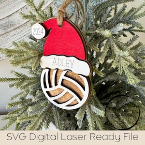 May include: A wooden Christmas bauble shaped like a volleyball with a red Santa hat on top. The bauble is personalised with the name "ADLEY" and the year "2024".