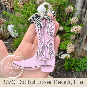 May include: Pink wooden cowboy boot ornament with a white and black chevron ribbon. The boot has a white outline and is ready to be laser cut.