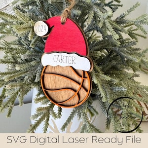 May include: A wooden Christmas bauble shaped like a basketball with a Santa hat on top. The basketball is brown with orange stitching. The Santa hat is red with a white trim. The bauble has the name "Carter" and the year "2024" on it.