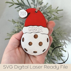 May include: A white wooden ornament shaped like a snowman wearing a red Santa hat with the name "GABRIEL" written on it. The ornament also has a small white circle with the year "2024" written on it.