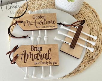 May include: Two wooden golf ball holder tags with personalized text. The top tag reads "Gordon McFarlane Best Grandpa by par" and the bottom tag reads "Brian Amaral Best Daddy by par".