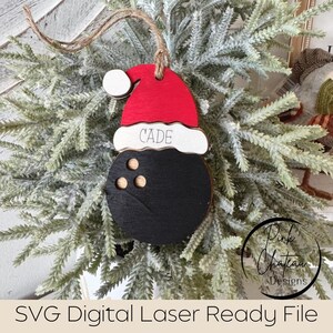 May include: A black and white bowling ball bauble with a red and white Santa hat. The hat has the name "CADE" written on it.