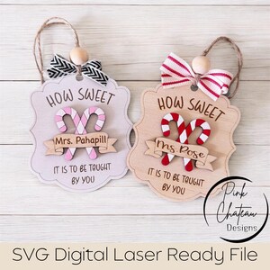 May include: Two wooden teacher appreciation ornaments. One is light gray with pink candy canes, the other is natural wood with red candy canes. Both say "How Sweet" and "It is to be taught by you."