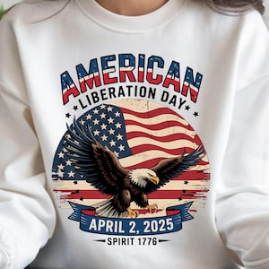 Könnte beinhalten: Weißer Pullover mit einem Vintage-Grafikdesign mit einer amerikanischen Flagge, einem Weißkopfseeadler und dem Text "AMERICAN LIBERATION DAY APRIL 2, 2025 SPIRIT 1776".