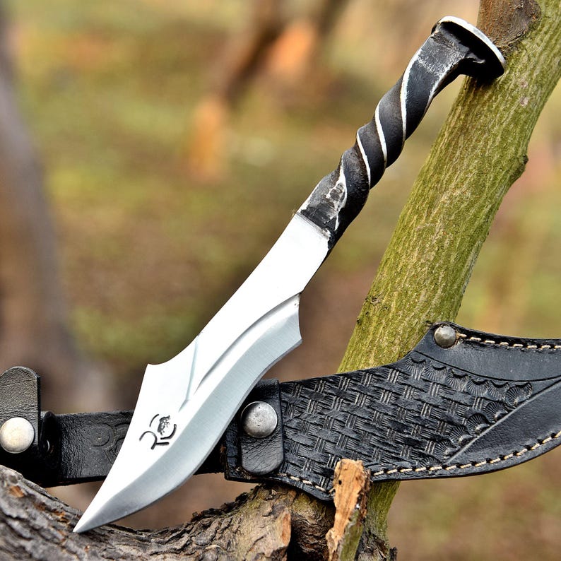 May include: A handcrafted knife with a twisted metal handle and a silver blade. The blade is resting on a black leather sheath with a woven pattern. The knife has a unique design and is likely used for outdoor activities.