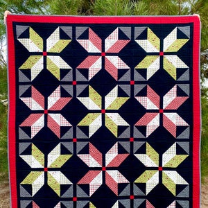 Könnte beinhalten: Eine Steppdecke mit schwarzem Hintergrund und einem sich wiederholenden Muster aus roten, weißen und grünen Sternen. Die Steppdecke ist mit einem roten Rand eingefasst.