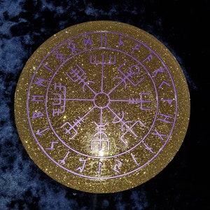 May include: A gold glitter round coaster with a purple compass design and runes around the edge.