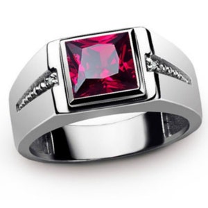 Peut inclure: Bague en argent avec une pierre précieuse rouge foncé carrée au centre. La bague présente un design moderne avec de petites pierres claires incrustées dans la bande de chaque côté de la pierre précieuse. Un bijou classique.