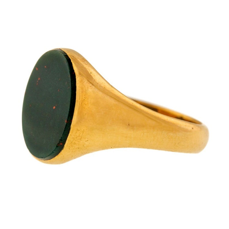 K&ouml;nnte beinhalten: Ein goldener Siegelring mit einem ovalen, dunkelgr&uuml;nen Stein, der mit roten Flecken durchzogen ist. Der Ringreif und die Fassung sind aus poliertem, warmem Gold. Der Ring wird von der Seite gezeigt, um die Form des Steins und das Design des Rings hervorzuheben.