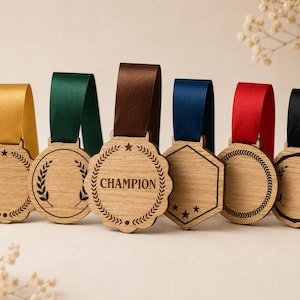Op de afbeelding: Zes houten medailles met kleurrijke linten. De medailles hebben verschillende vormen, waaronder een cirkel, een zeshoek en een geschulpte rand. Eén medaille zegt "Champion". Elke medaille heeft een lint in een andere kleur: geel, groen, bruin, blauw, rood en zwart.