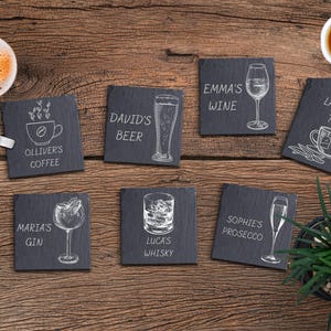 Könnte beinhalten: Satz von zehn schwarzen Schieferuntersetzern mit weißen Illustrationen von Getränken und den Namen der Getränke. Die Untersetzer zeigen Getränke wie Kaffee, Bier, Wein, Gin, Whisky, Prosecco und Tee.