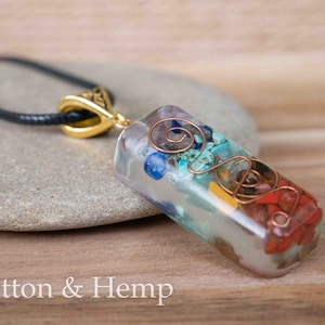 May include: A clear rectangular pendant necklace with a variety of colorful stones and copper wire swirls inside. The pendant is attached to a black cord.