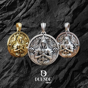 May include: Three silver pendants with a detailed warrior design. The pendants are in gold, silver, and bronze tones, each featuring a figure holding a sword. The pendants have a circular shape with intricate detailing and a loop for a chain. The Duende Silver logo is at the bottom.