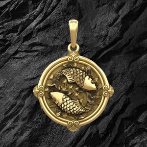 Puede incluir: Colgante dorado con dos peces en un dise&ntilde;o circular, representando el signo zodiacal de Piscis. El colgante tiene detalles intrincados y un borde decorativo, con un lazo en la parte superior para una cadena.