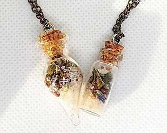 Könnte beinhalten: Eine goldene Kettenkette mit zwei kleinen Glasflaschen, die mit verschiedenen Kristallen, Kräutern und anderen natürlichen Elementen gefüllt sind. Die Flaschen sind mit einer silbernen Schlaufe an der Kette befestigt.