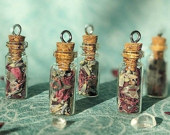 Puede incluir: Cinco pequeñas botellas de vidrio con tapones de corcho y tapas plateadas llenas de pétalos de rosa secos y cristales. Las botellas están dispuestas en fila sobre una superficie texturizada azul claro y verde.