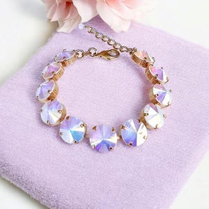 Op de afbeelding: Een gouden armband met een rij van iriserende witte kristallen. De armband heeft een sluiting.