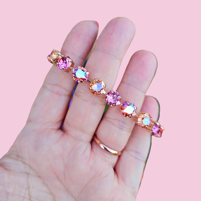 Op de afbeelding: Een delicate armband met een ketting van iriserende roze en perzikkleurige kristallen, gezet in ros&eacute;goud.