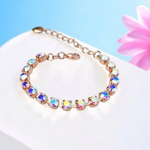 May include: A rose gold bracelet with a delicate chain and iridescent rhinestones. The bracelet is on a white surface.